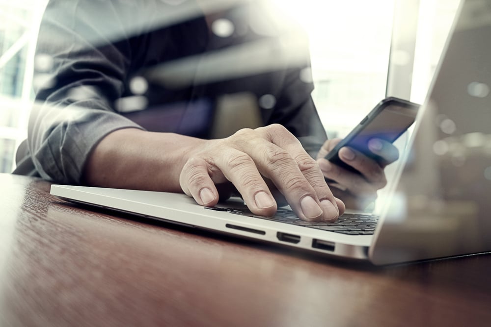 designer hand working and smart phone and laptop on wooden desk in office with london city background-1